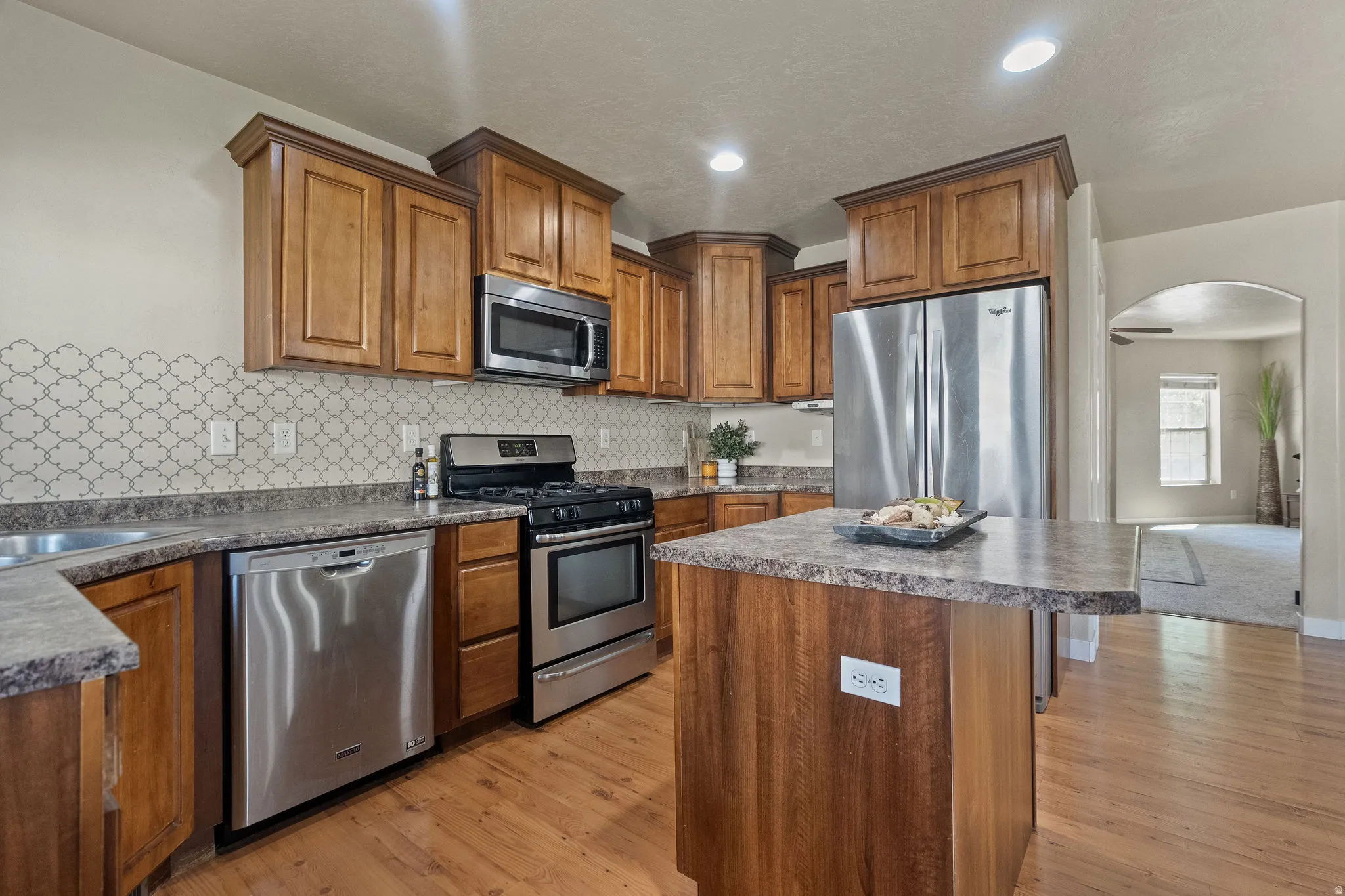 Well-appointed kitchen featuring wood cabinetry, stainless steel appliances, patterned backsplash, and an extended island with power outlet