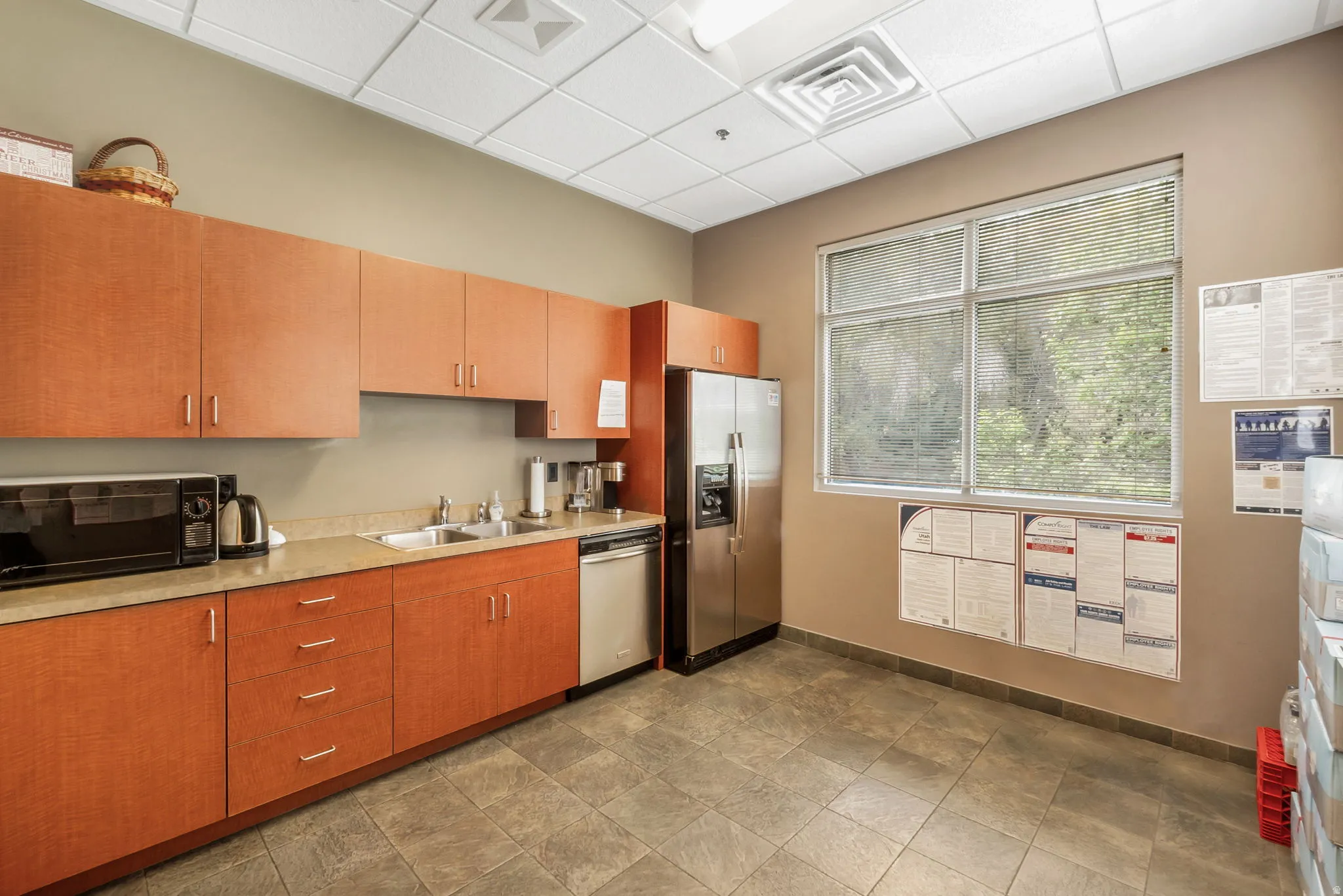 Kitchenette featuring wood-finish cabinetry, stainless steel appliances, a double basin sink, and a large window