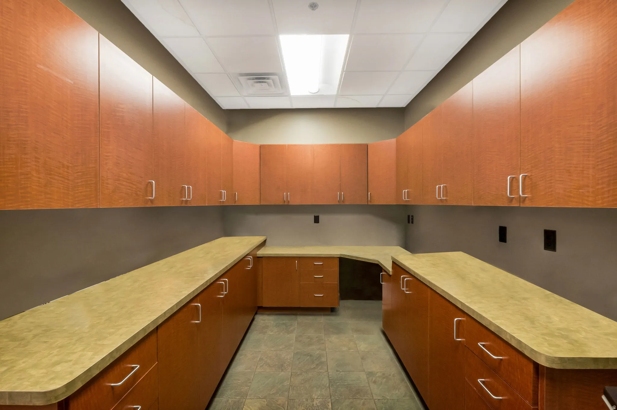 Extensive cabinetry and countertops featuring wood-finish lower and upper cabinets, light-toned countertops, and tile flooring