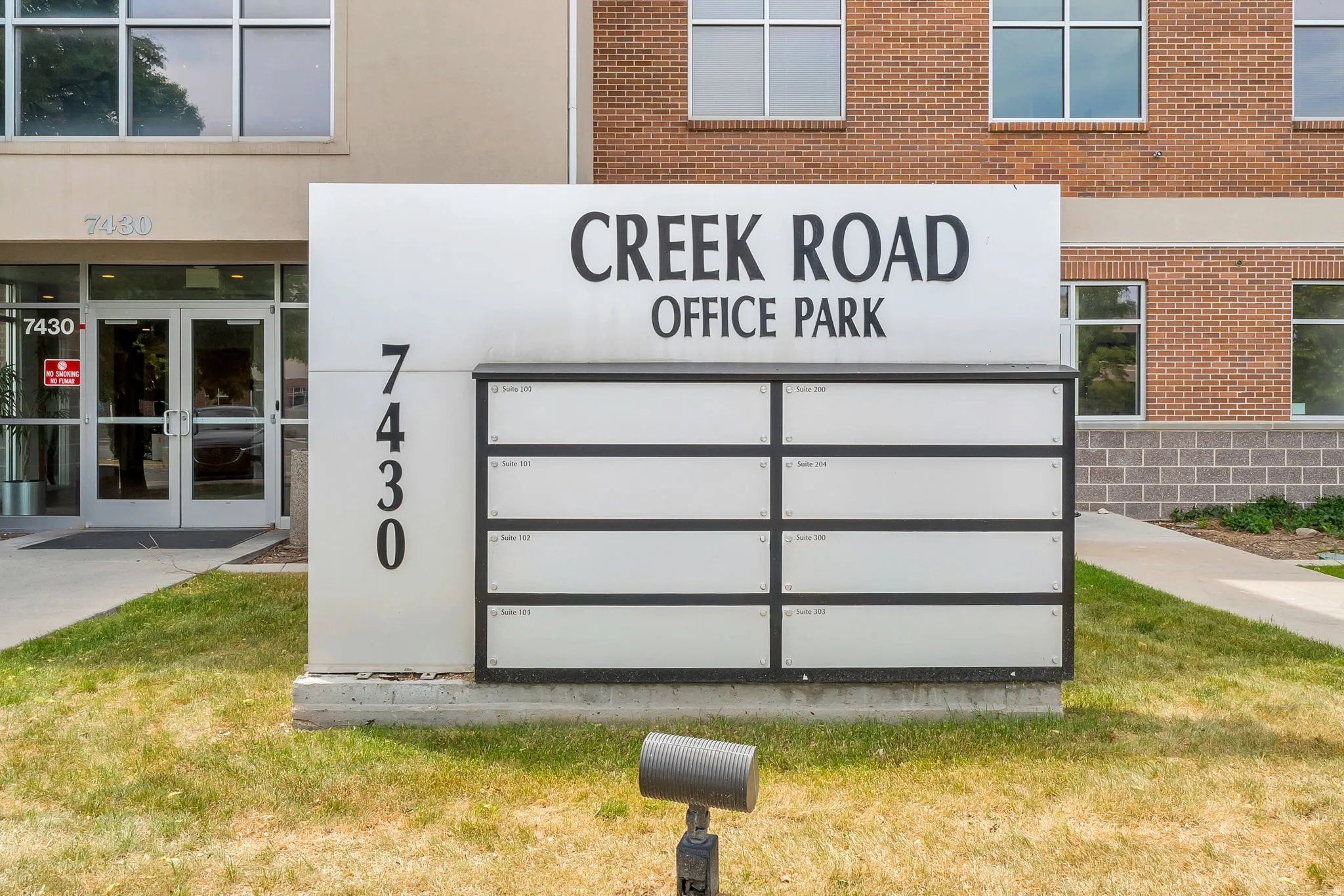 Creek Road Office Park monument sign with street address 7430, featuring individual tenant directories, a brick facade building, and a glass-paneled entrance
