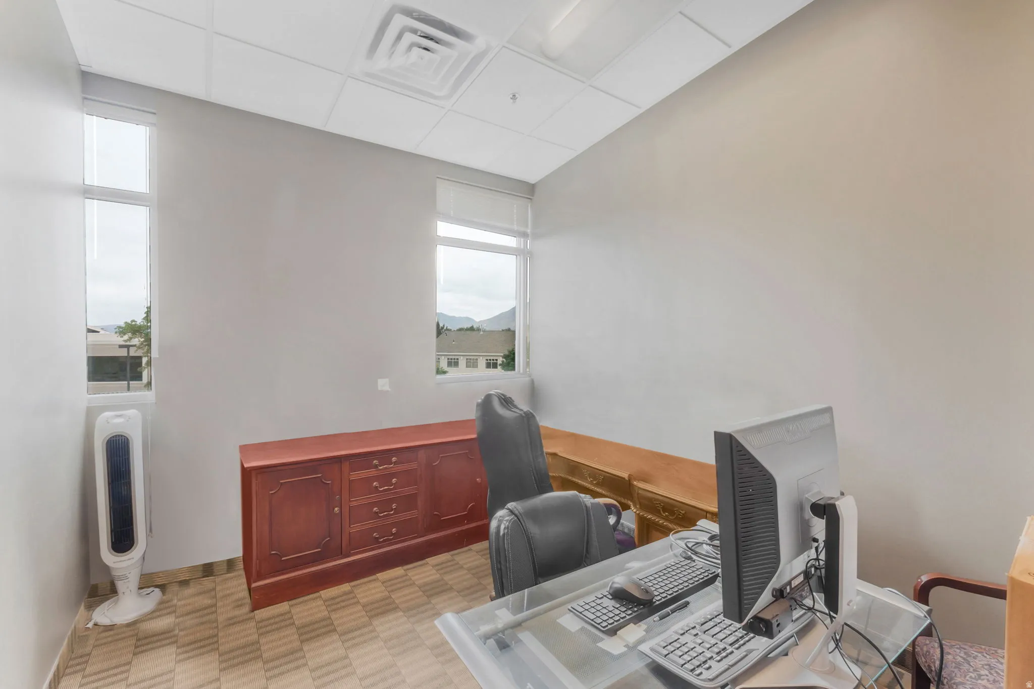 Neutral-toned interior room featuring two windows and a drop ceiling with recessed lighting