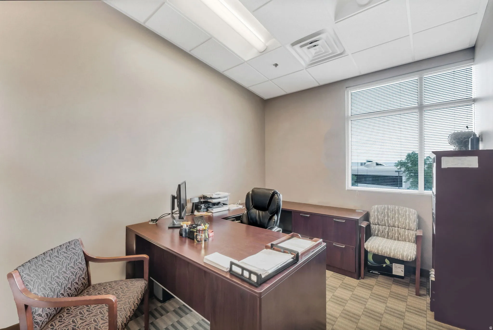 Office space featuring a drop ceiling with recessed lighting, neutral wall paint, and a large window with blinds