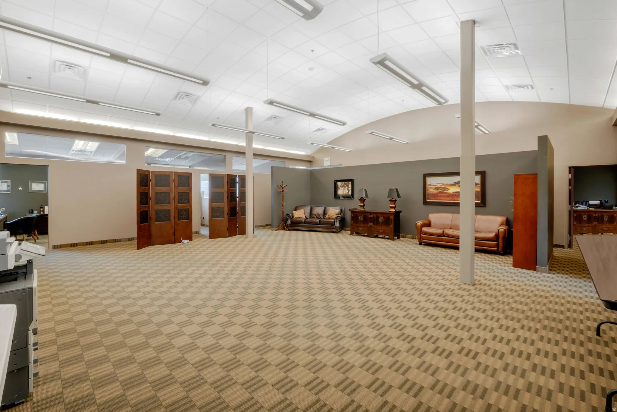 Expansive open-concept room featuring patterned carpet flooring, a suspended ceiling with integrated linear lighting, and clerestory windows