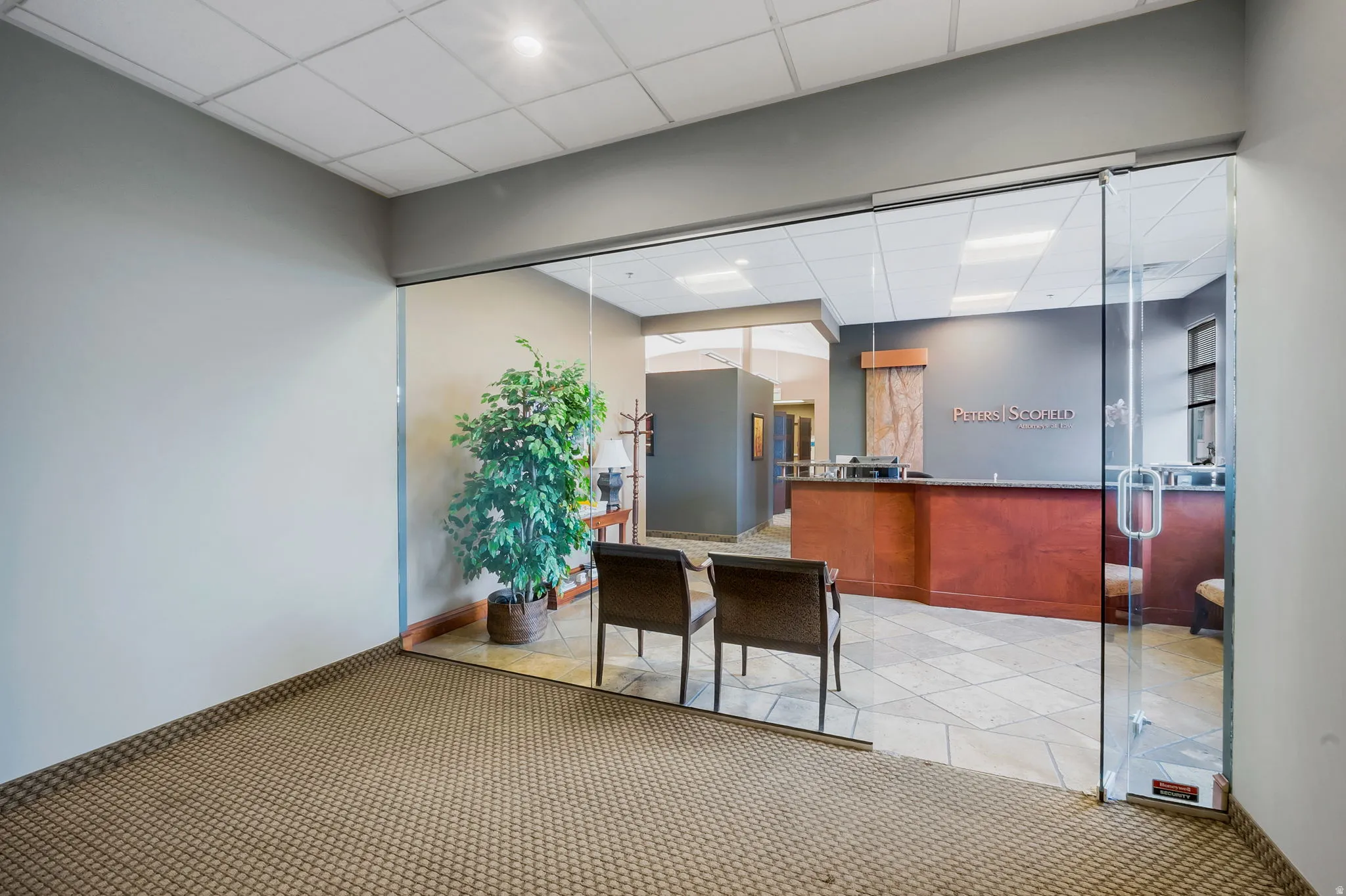Glass entry door opening to a reception area featuring a wood-finish desk and neutral-toned tile flooring