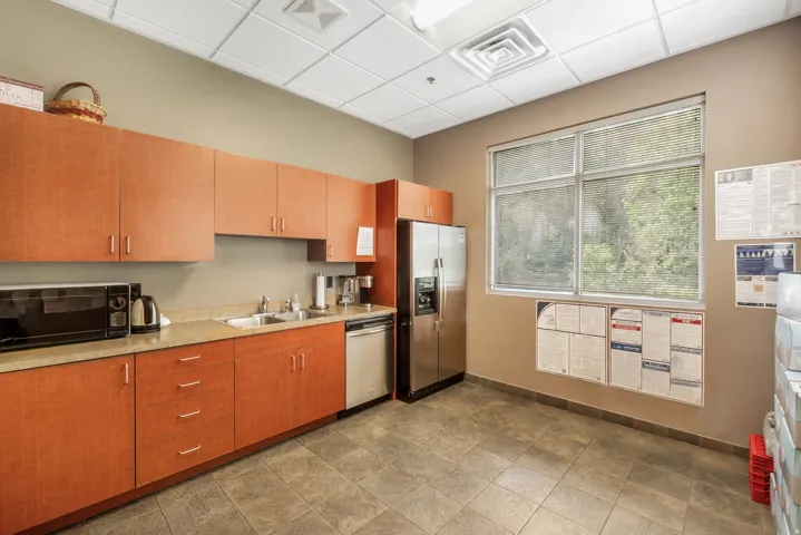 Kitchenette featuring wood-finish cabinetry, stainless steel appliances, a double basin sink, and a large window