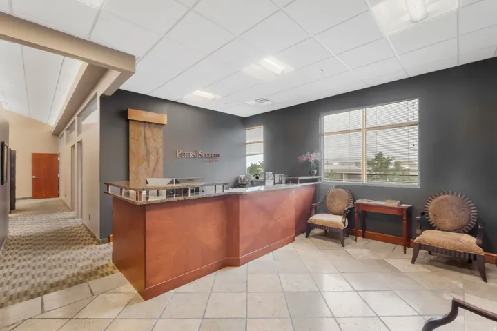 Spacious reception area featuring a wood-finish reception desk with a stone countertop, an integrated water feature, large windows with horizontal blinds, and tile flooring