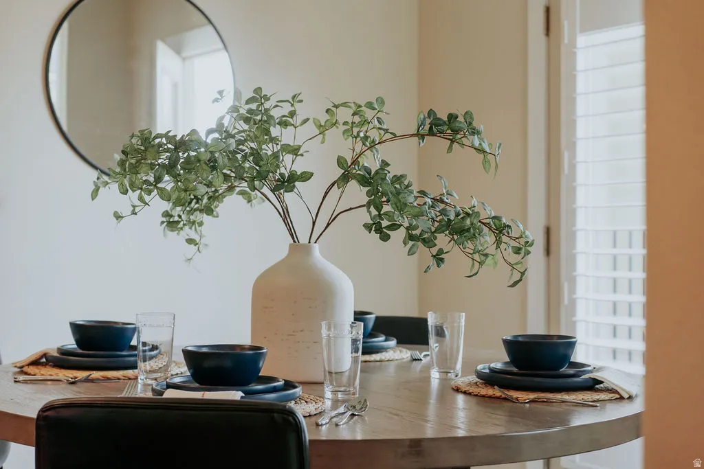 Dining area featuring a wood-finish table, plantation shutters, and a wall-mounted round mirror