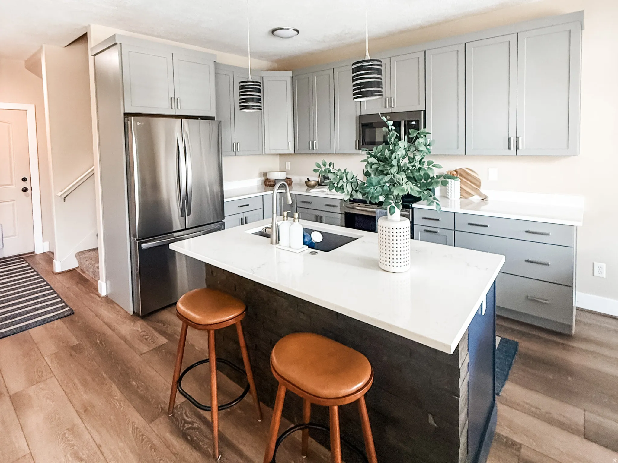 Modern kitchen featuring a central island with an integrated sink, white countertops, and wood-finish flooring