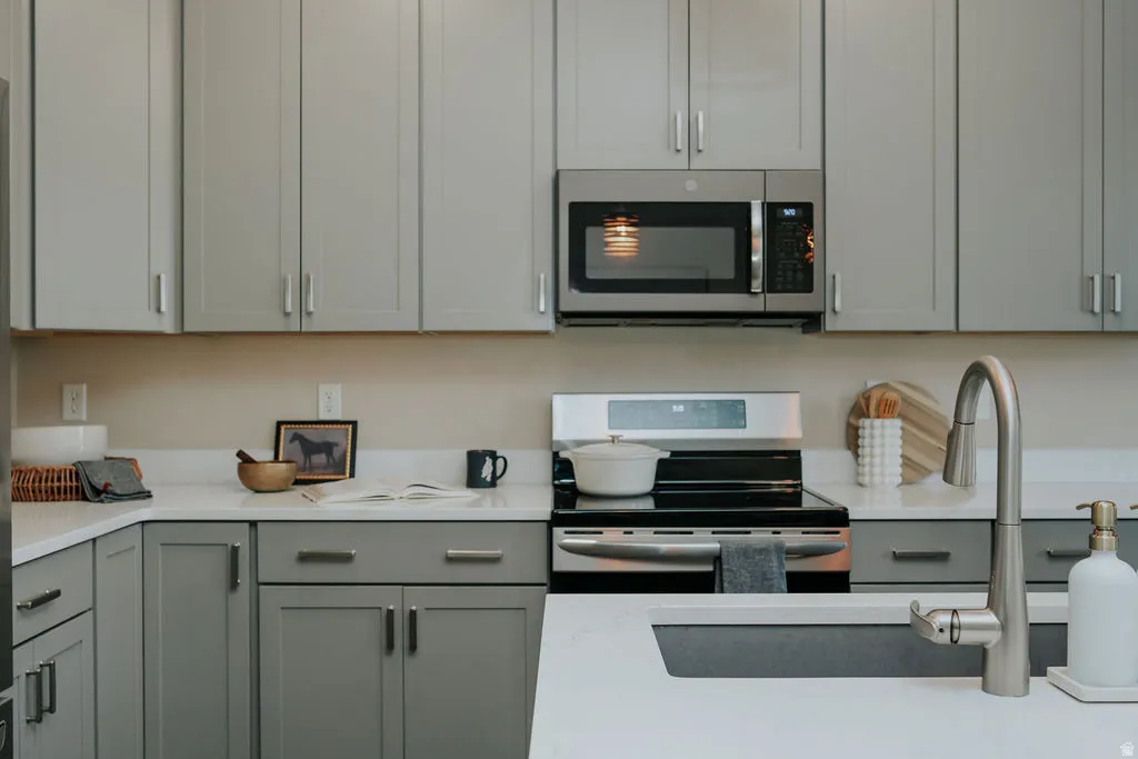 Modern kitchen featuring grey shaker-style cabinetry, white countertops, and stainless steel appliances