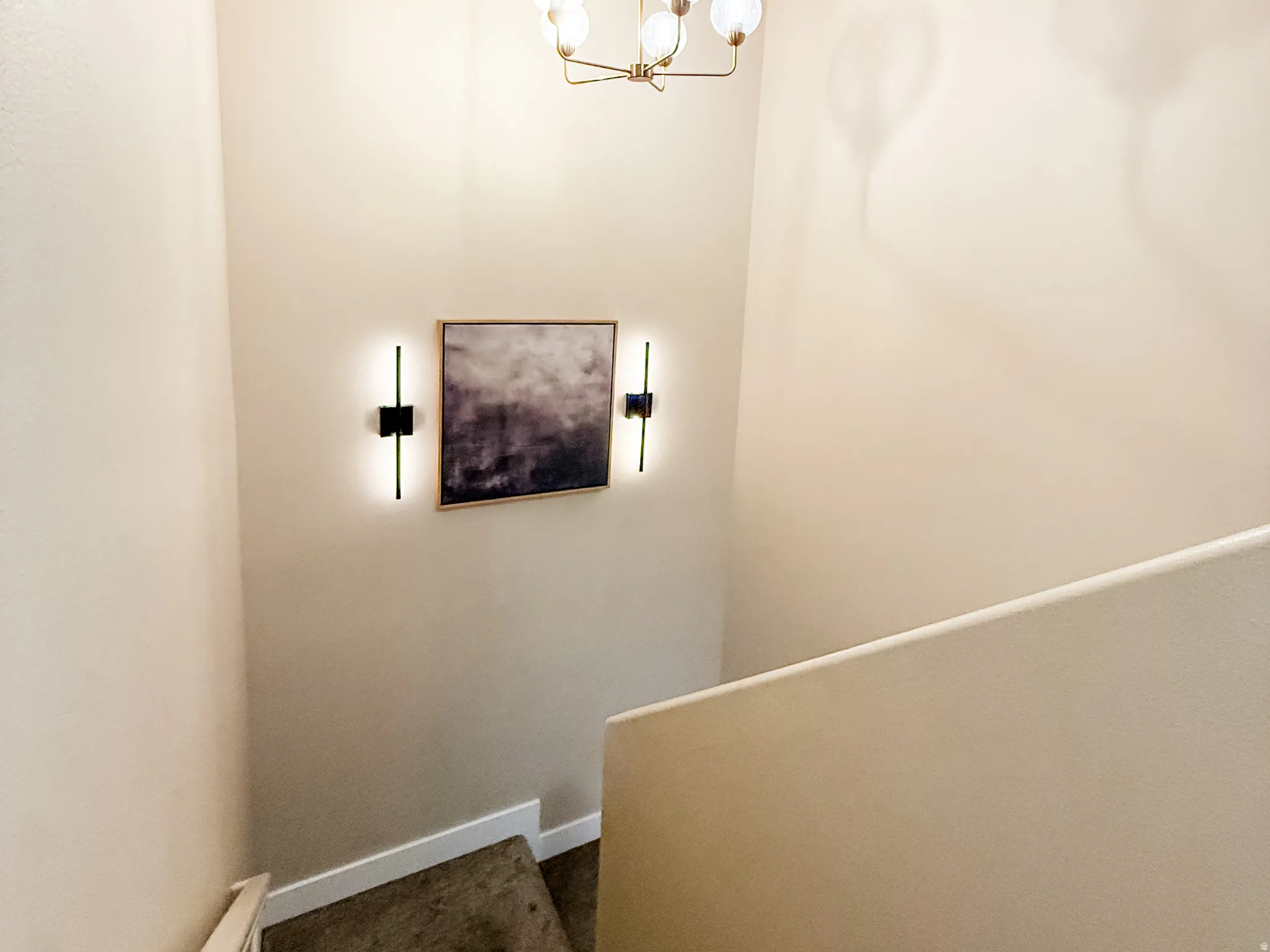Stairway featuring carpeted treads, a plaster half-wall, and a ceiling-mounted chandelier with globe lights