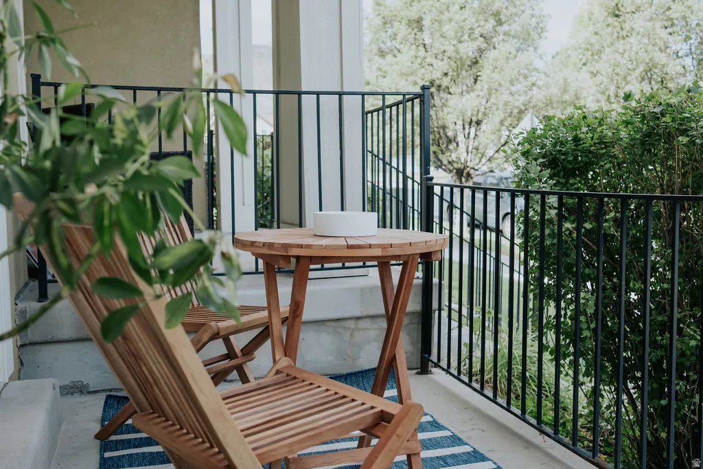 Front porch with a black metal railing, concrete flooring, and a view of surrounding greenery