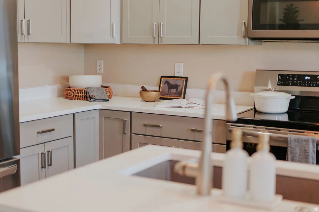 Modern kitchen featuring light gray shaker-style cabinetry, stainless steel appliances, a built-in microwave, and solid surface countertops