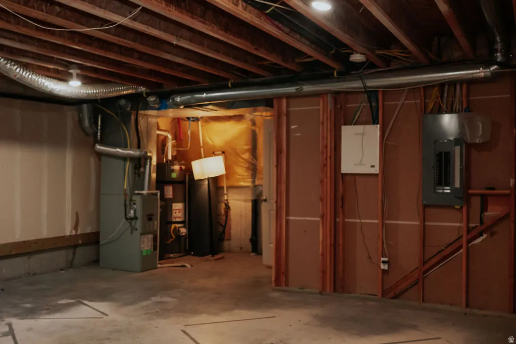 Unfinished basement space featuring exposed wood joists, concrete flooring, and visible utility systems including a furnace, water heater, and electrical panels