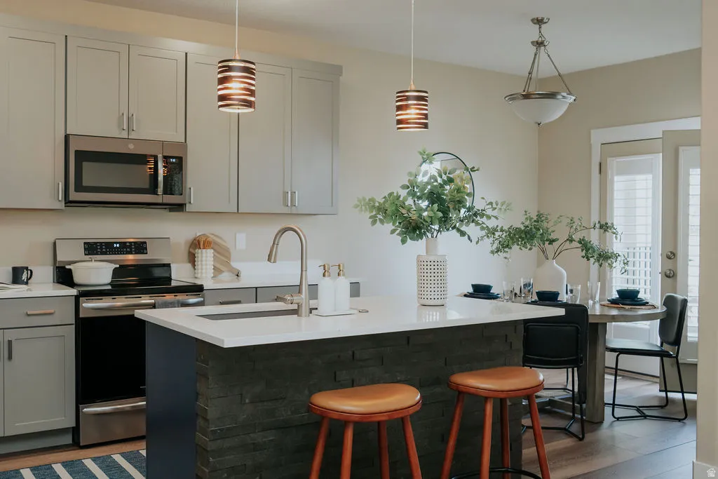 Kitchen featuring light gray cabinetry, stainless steel appliances, a white countertop island with stone veneer, and wood-finish flooring