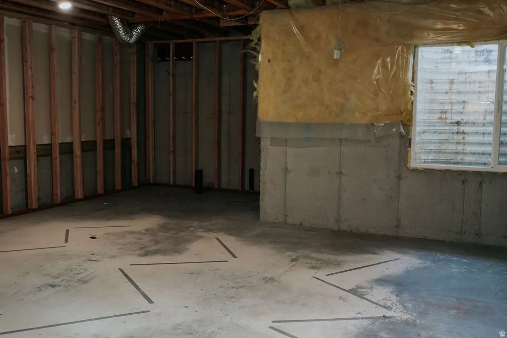 Unfinished basement with exposed wood framing, concrete foundation walls, and a visible window with horizontal blinds