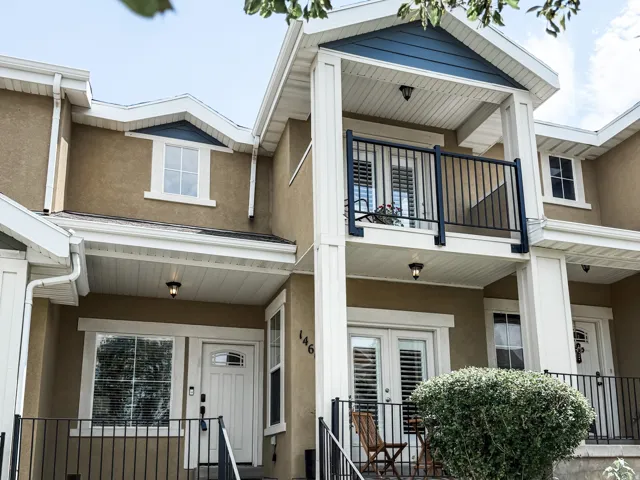 Stucco exterior with white trim, featuring a second-story balcony with black railings, a ground-level covered porch with white columns, and a dormer window with blue siding accent