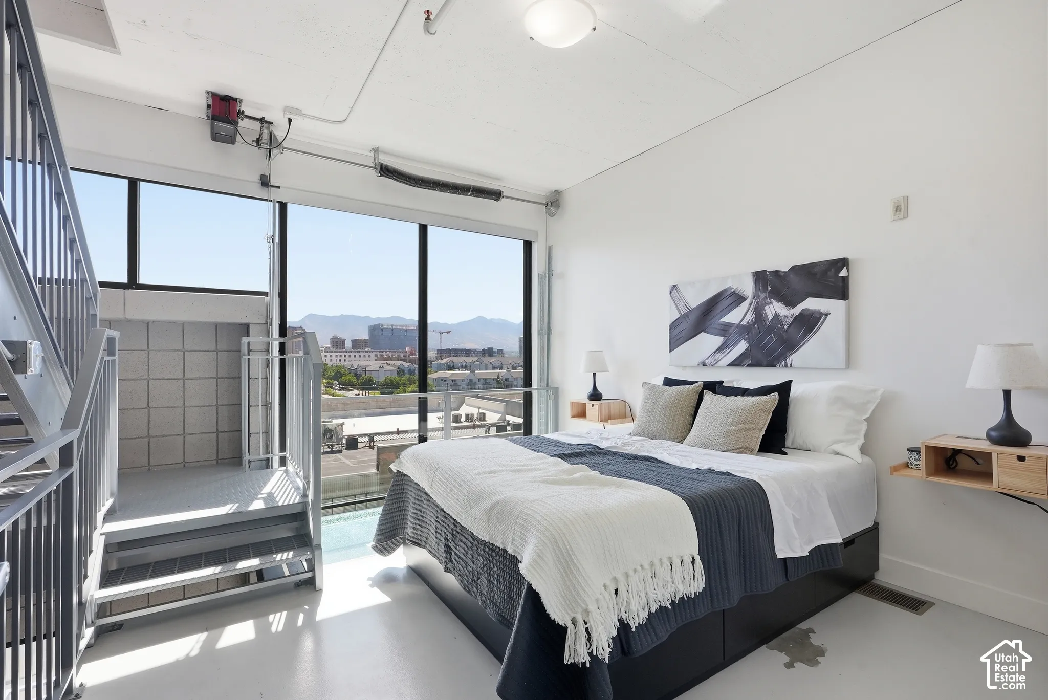 Expansive windows with mountain backdrop, industrial-style staircase and railing, white painted concrete flooring, recessed lighting, and high ceilings
