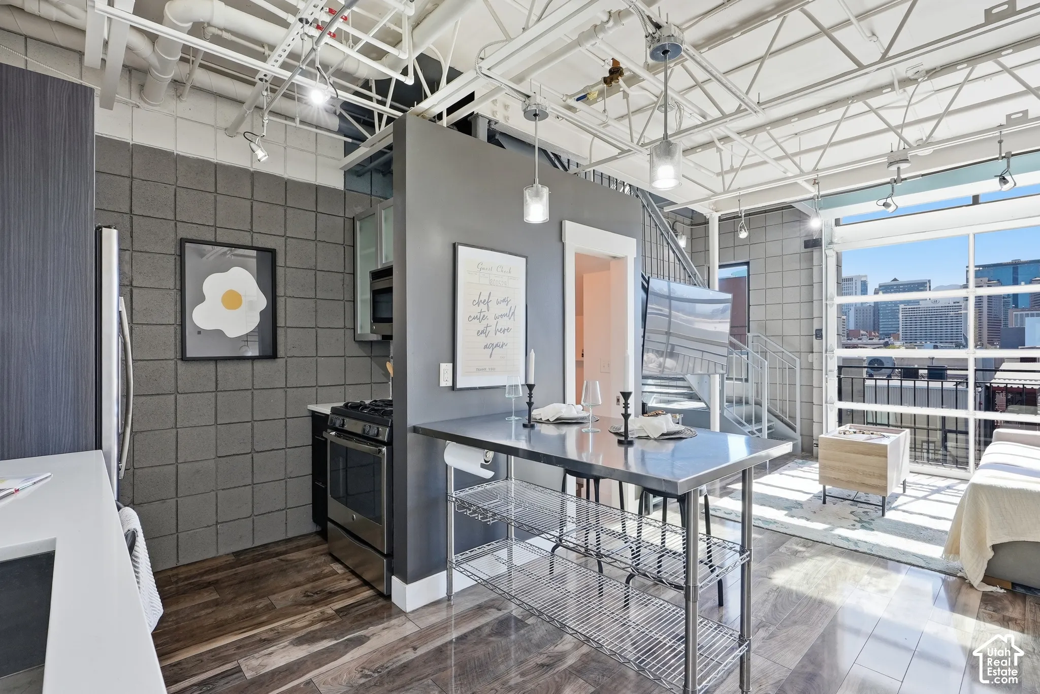 Open-concept living space featuring wood-finish flooring, exposed white ceiling trusses, and a full wall of industrial-style windows