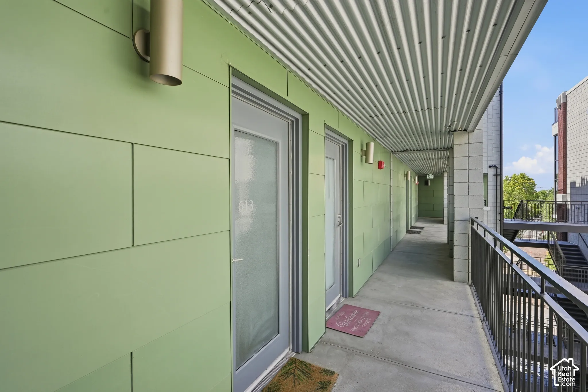 Open-air corridor featuring green paneling, corrugated metal ceiling, concrete flooring, and metal railings