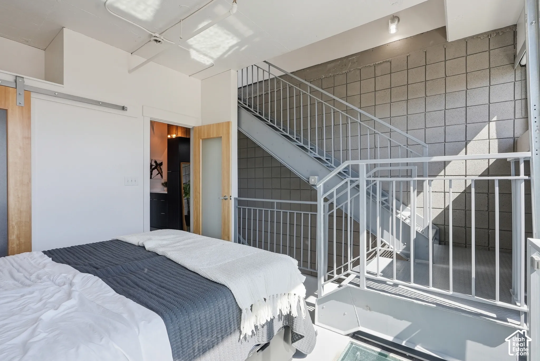 Exposed metal staircase with square grid wall detailing, light wood-finish barn door, and a frosted glass panel door