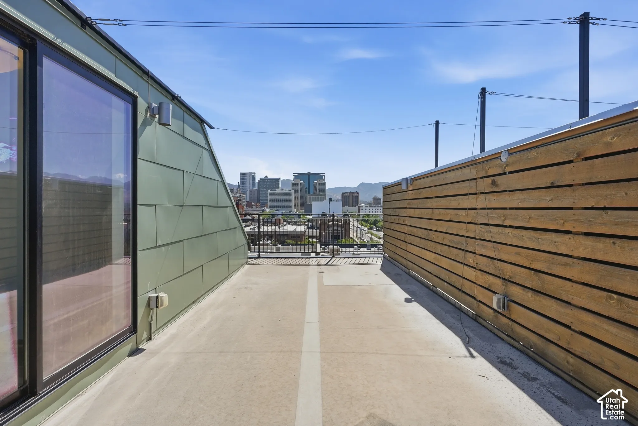 Rooftop deck featuring a concrete surface, green paneled siding, and a horizontal wood slat privacy wall