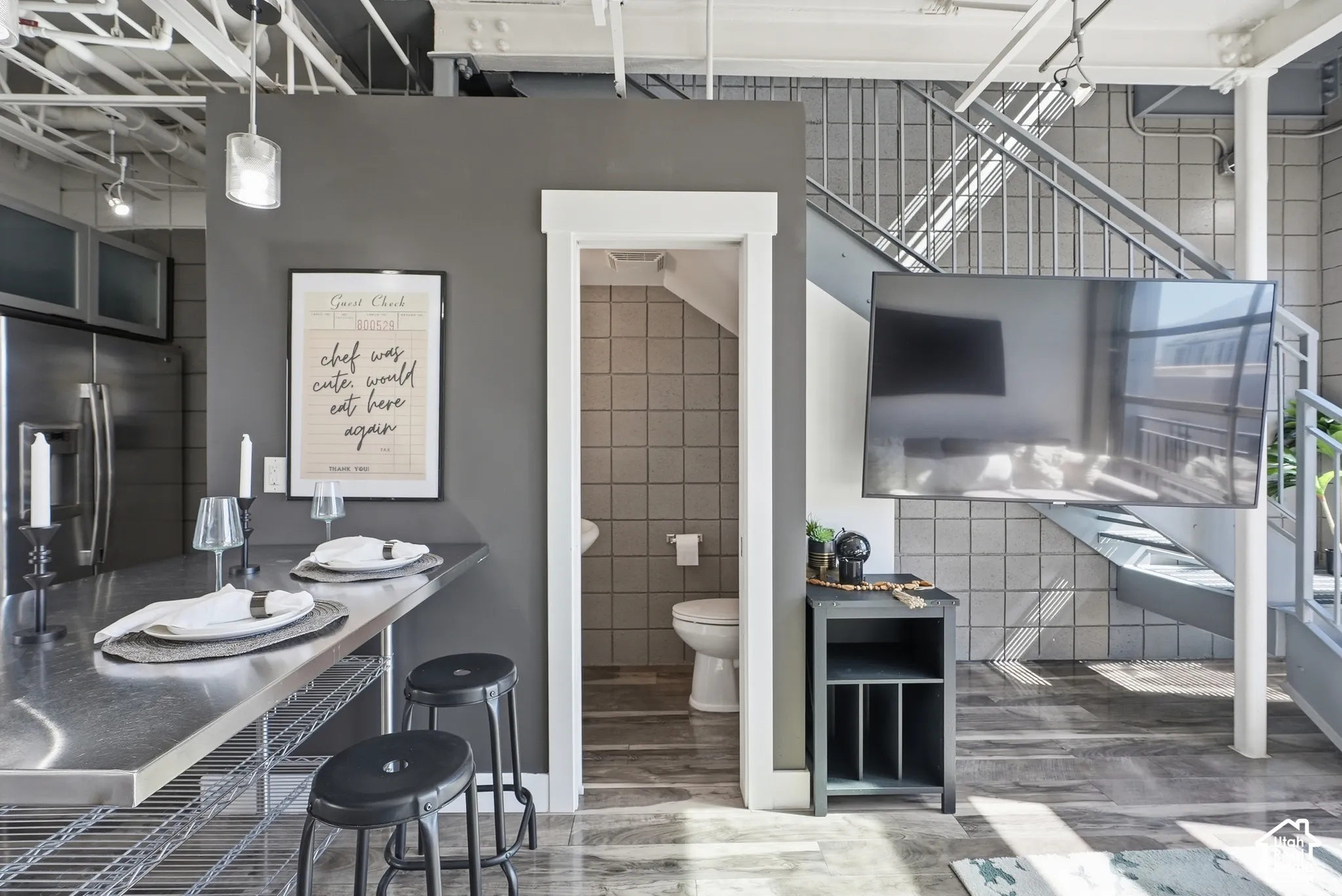 Open-concept living space featuring a stainless steel kitchen island with seating, exposed industrial-style ceiling beams, a contemporary open staircase, and wood-finish flooring
