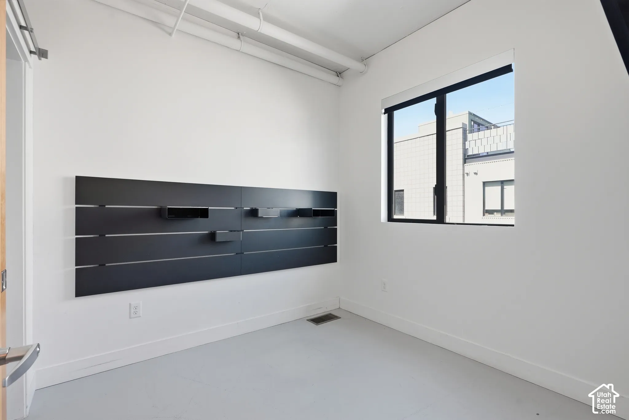 Room featuring a wall-mounted shelving unit, an exposed ceiling duct, and a window with black trim