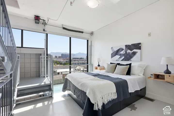 Expansive windows with mountain backdrop, industrial-style staircase and railing, white painted concrete flooring, recessed lighting, and high ceilings