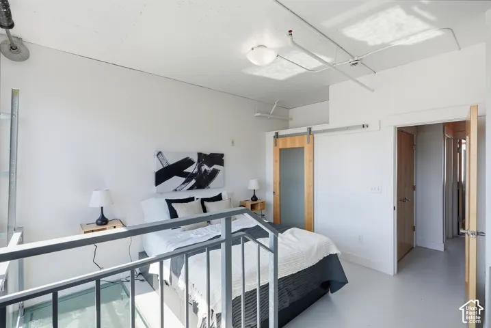 Loft bedroom featuring a barn door with frosted glass panel, exposed ceiling conduits, white walls, and light-toned flooring