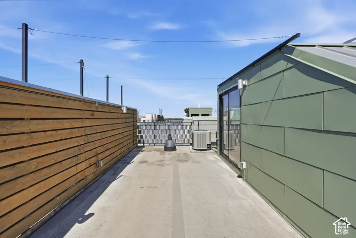 Rooftop deck featuring a concrete surface, a wood-slat privacy wall, and a green paneled structure with sliding glass doors