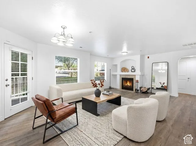 Living space with wood-finish flooring, a fireplace with a stone surround, and an arched entryway