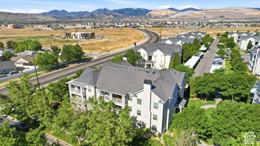 Multi-story residential building with light-colored siding, dark shingle roofing, multiple balconies, and mature landscaping