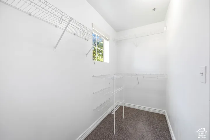 Walk-in closet featuring white wire shelving, a window with exterior foliage, white baseboards, and dark gray carpet flooring