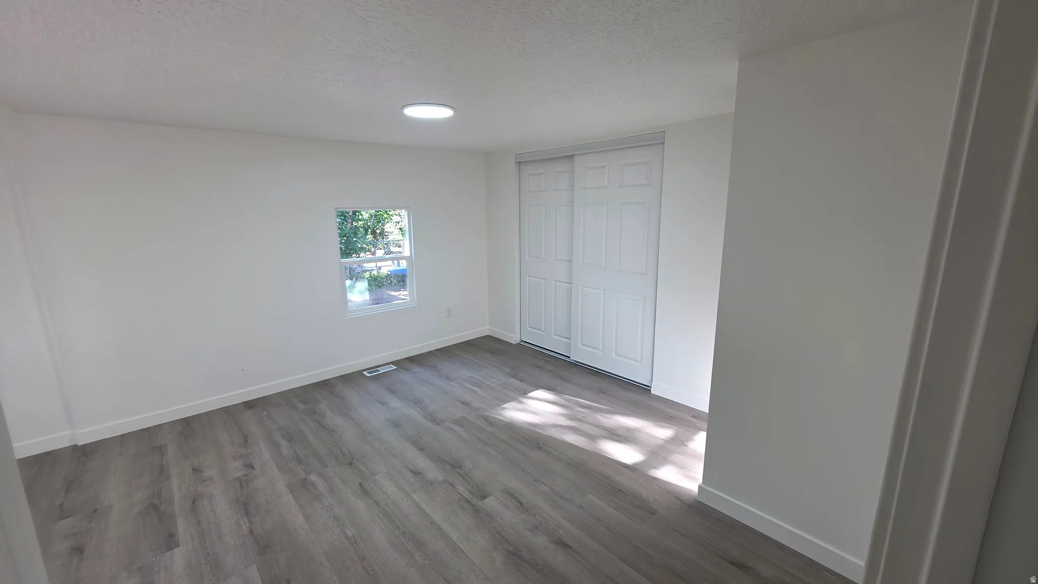 Spacious interior room featuring wood-finish flooring, white walls, and a recessed ceiling light