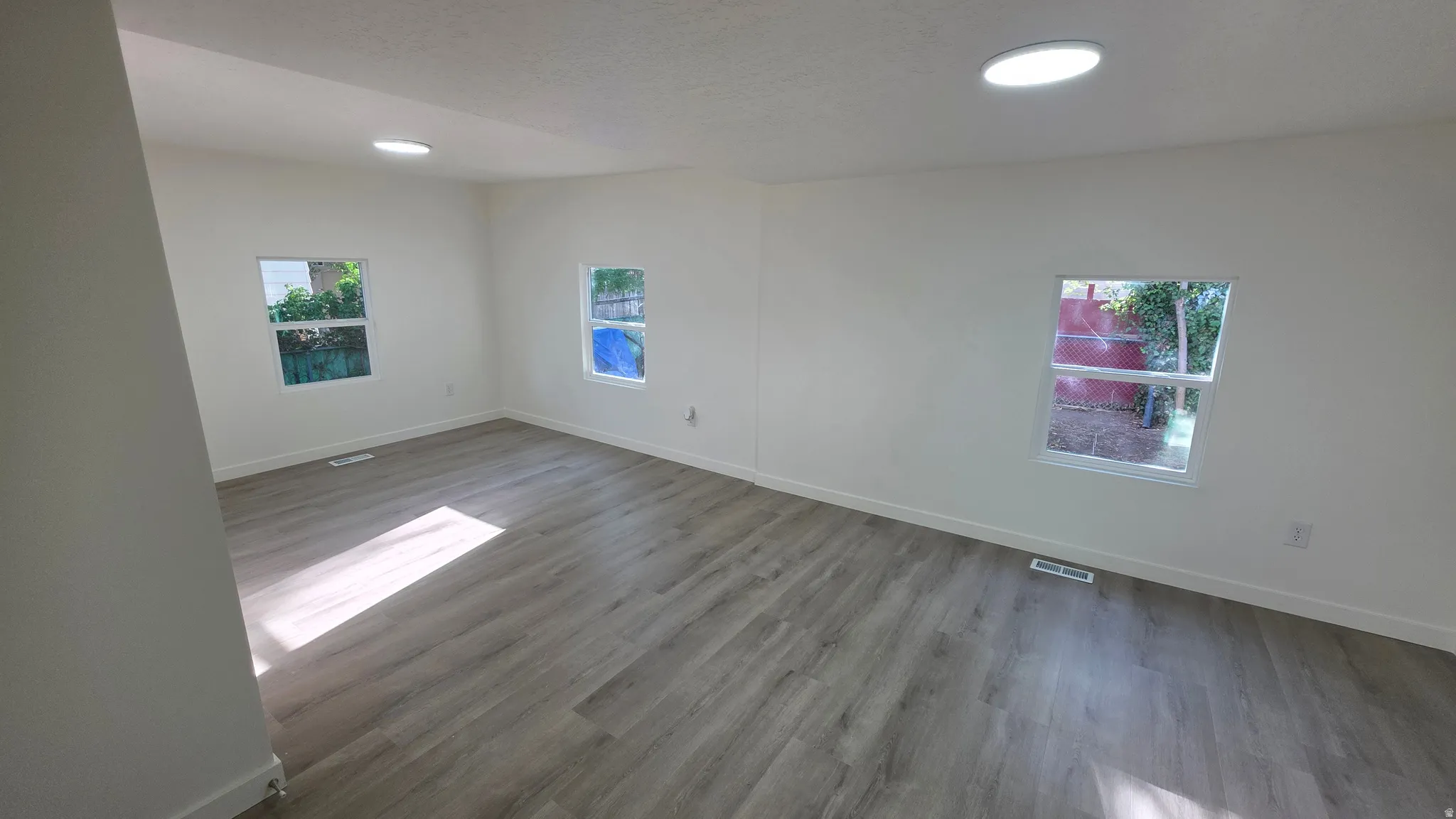 Spacious room featuring light wood-finish flooring, white walls, multiple windows, and recessed ceiling lighting