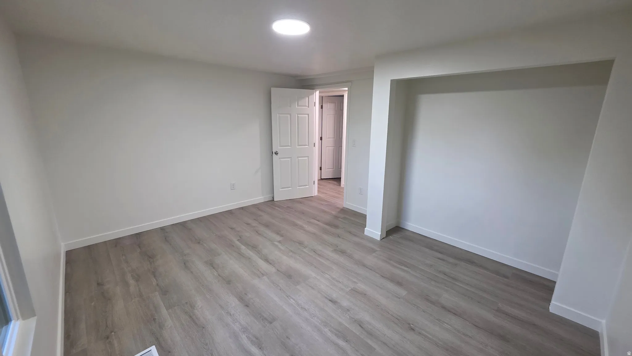 Spacious room featuring wood-finish flooring, a built-in alcove, and a contemporary ceiling light fixture