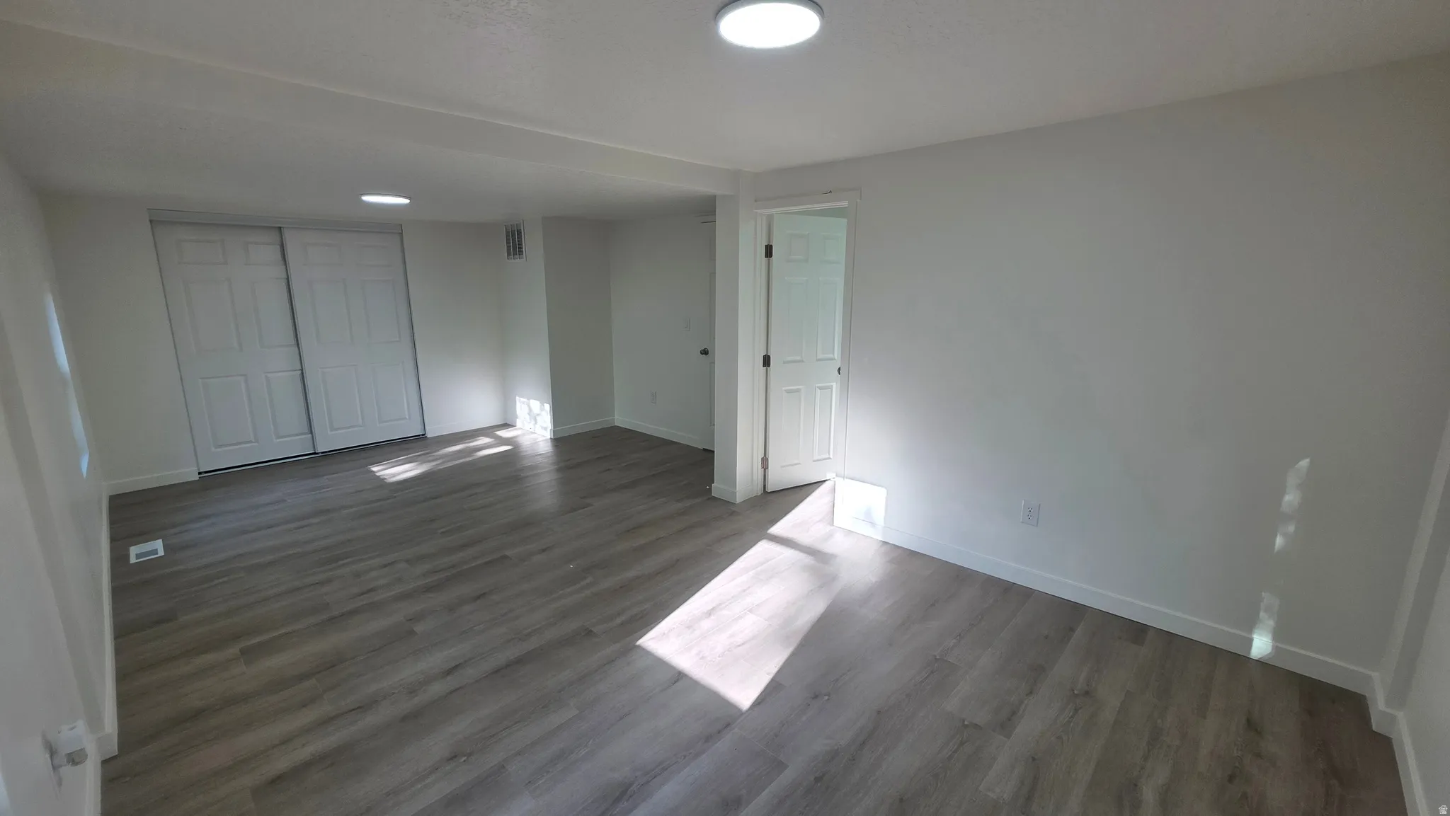 Spacious room featuring wood-finish flooring, white walls, and a ceiling-mounted light fixture