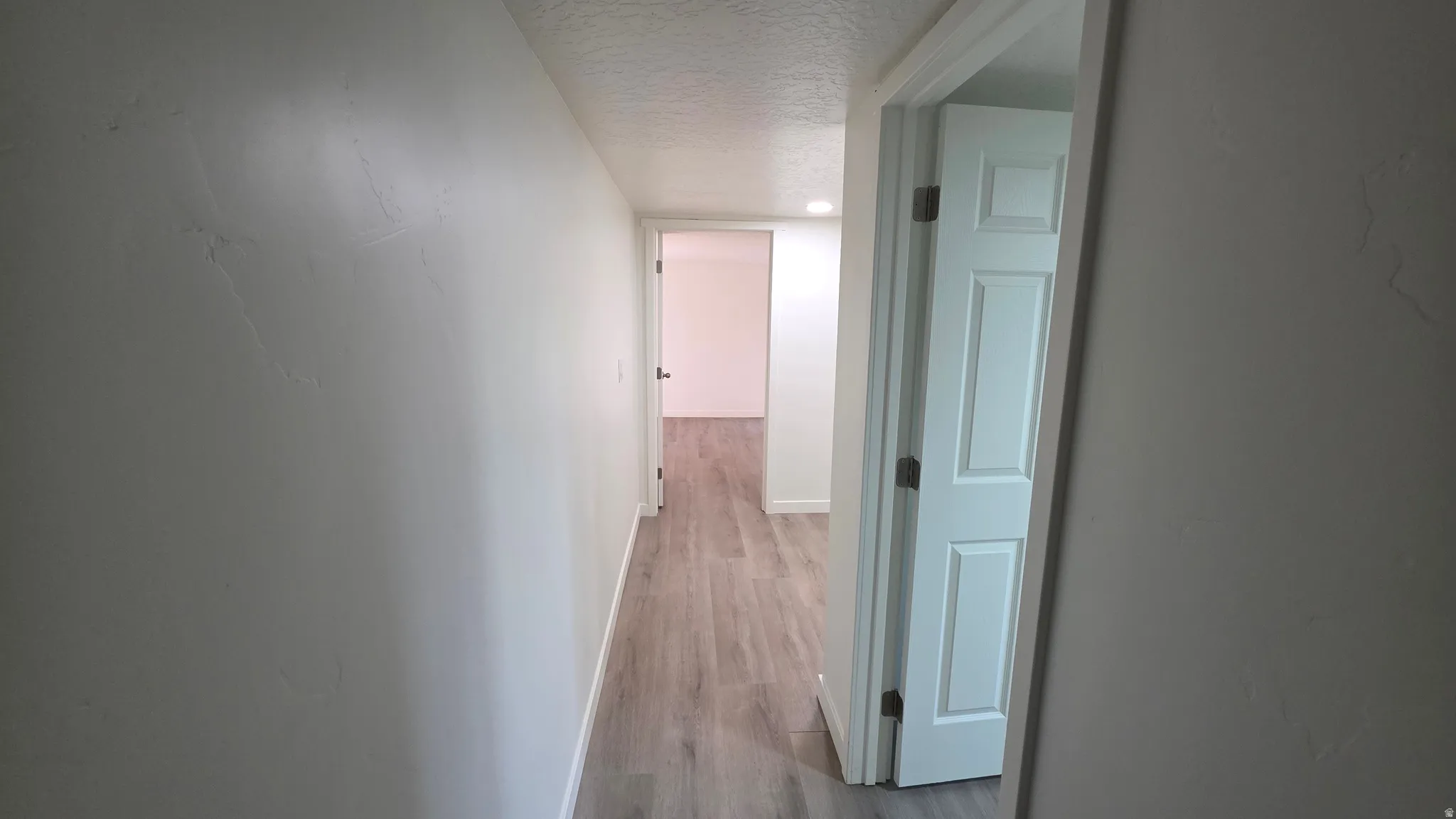 Hallway featuring light-toned wood-finish flooring, white walls, and white paneled doors