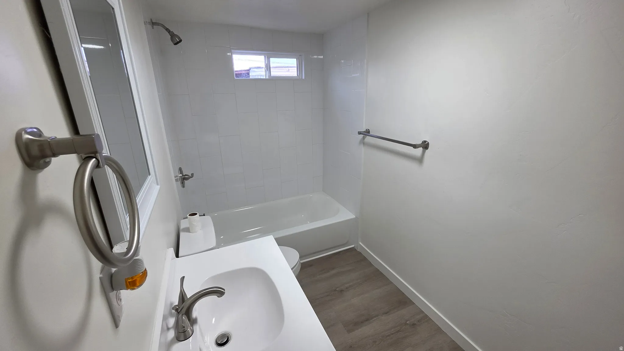 Bathroom featuring a white vanity with integrated sink, brushed nickel faucet, a full-size bathtub with shower, white subway tile surround, and wood-finish flooring