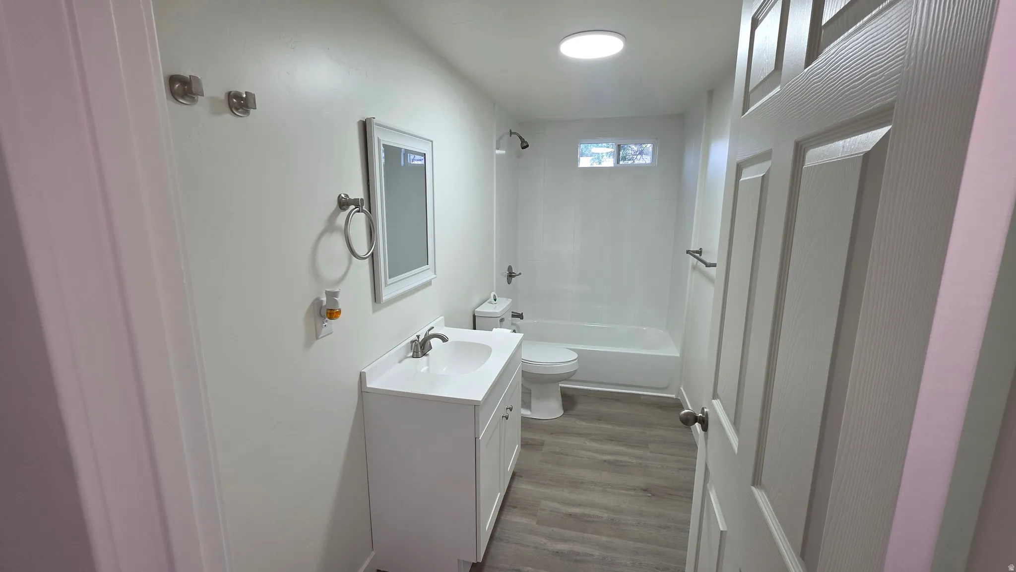 Clean bathroom featuring a white vanity with integrated sink, chrome fixtures, and wood-finish flooring
