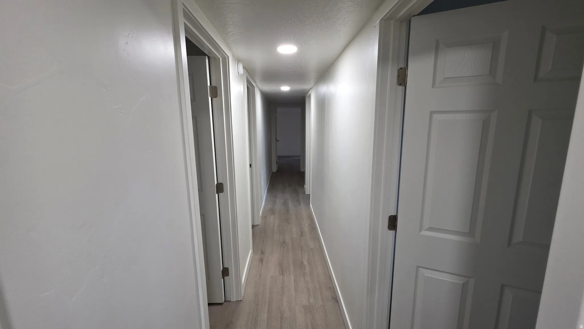 Hallway featuring wood-finish flooring, recessed lighting, white walls, and multiple panel doors