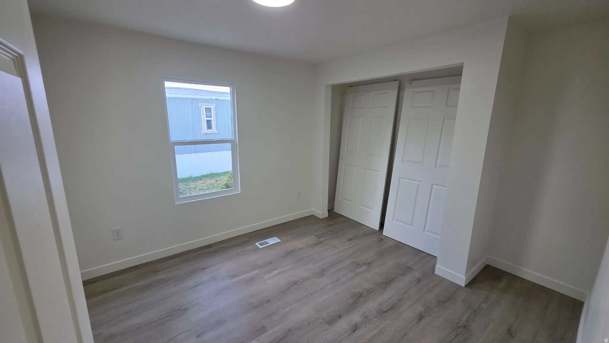 Spacious room featuring light wood-finish flooring, white walls, and a single window with white trim