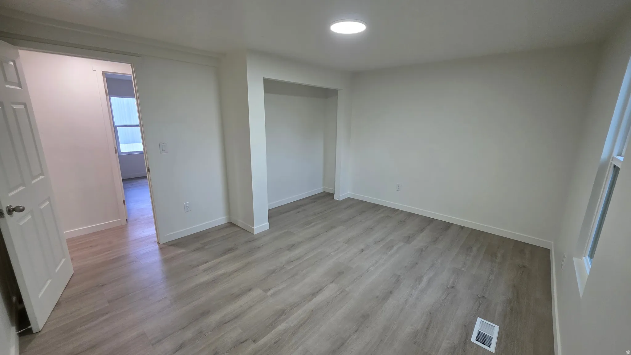 Spacious room featuring wood-finish flooring, white baseboards, and bright white walls