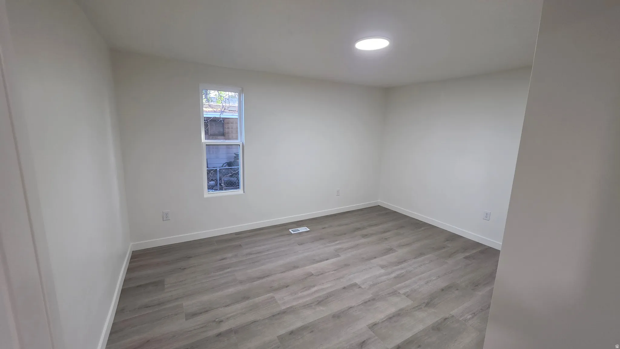 Light-filled room featuring wood-finish flooring, a single window, recessed lighting, and white walls