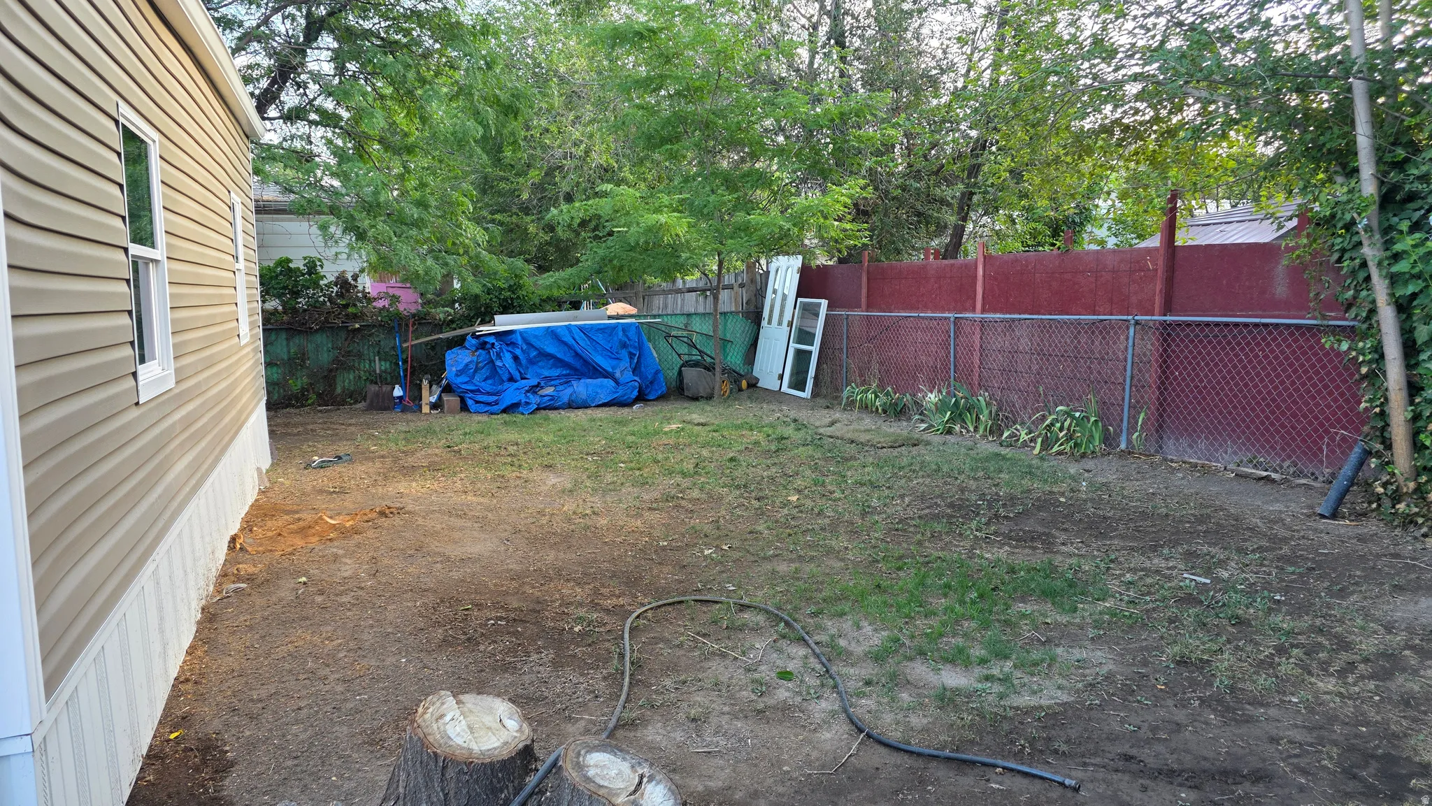 Side exterior with horizontal tan siding, white trim, and a fenced backyard featuring a chain-link and solid red fence