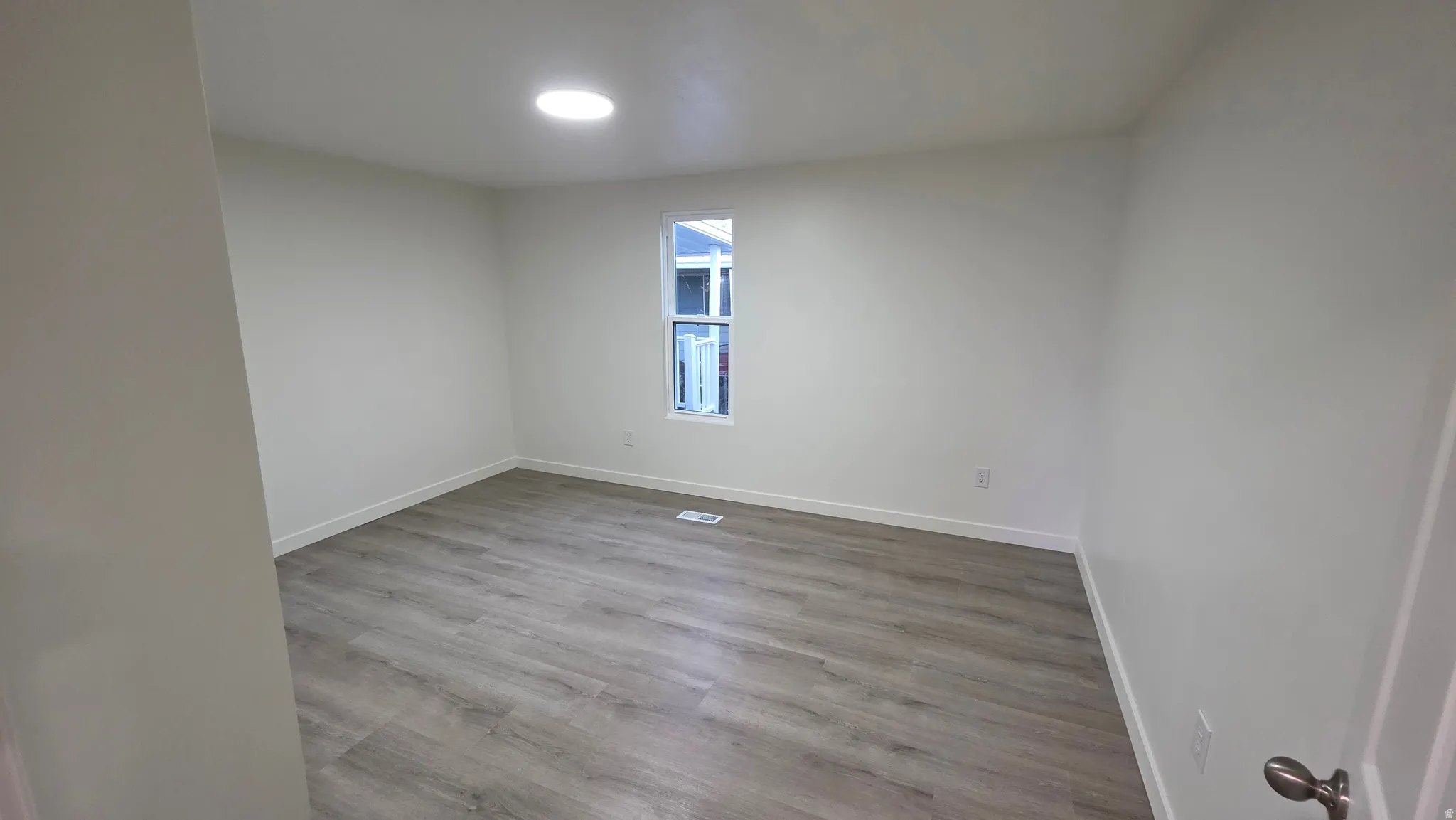 Bright room featuring light wood-finish flooring, white walls, a single window, and a circular ceiling light fixture