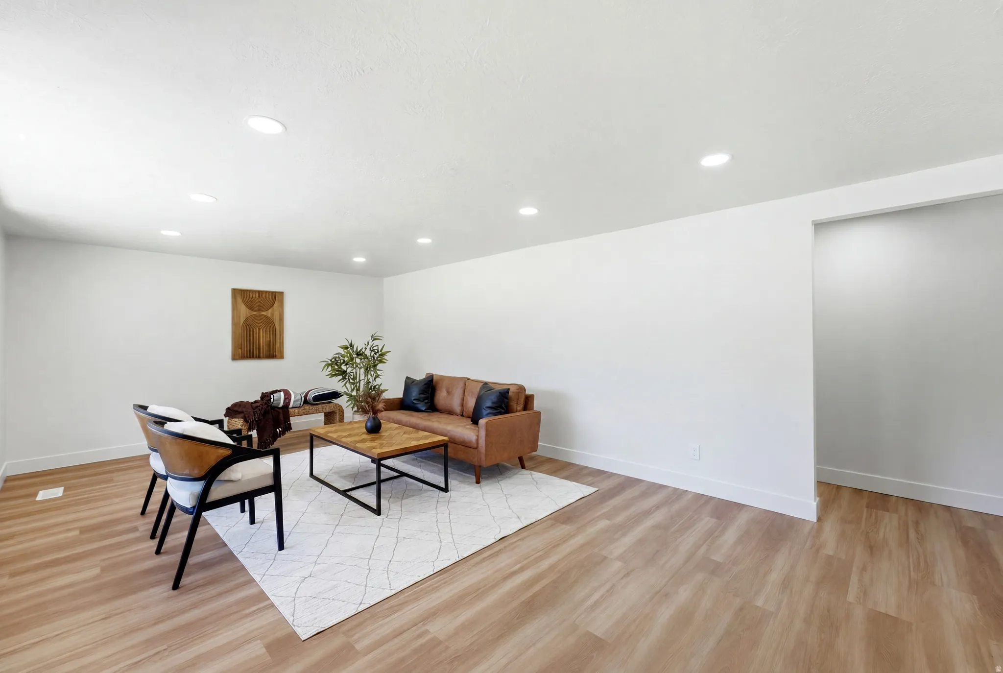 Spacious open living area featuring wood-finish flooring, recessed lighting, white walls, and white baseboards