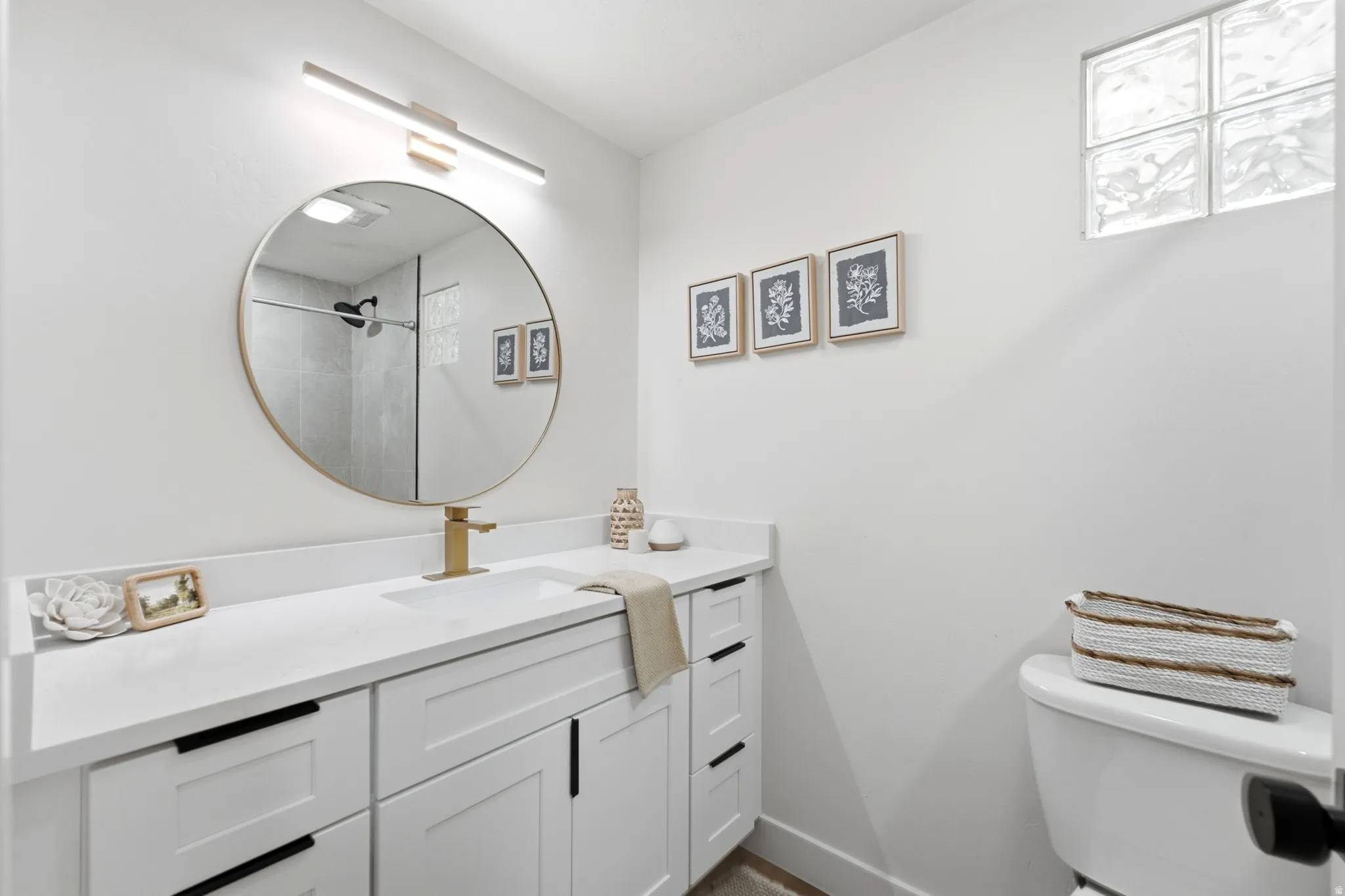 Contemporary vanity featuring white shaker-style cabinetry with matte black hardware, a pristine white countertop, and a sleek gold-toned faucet