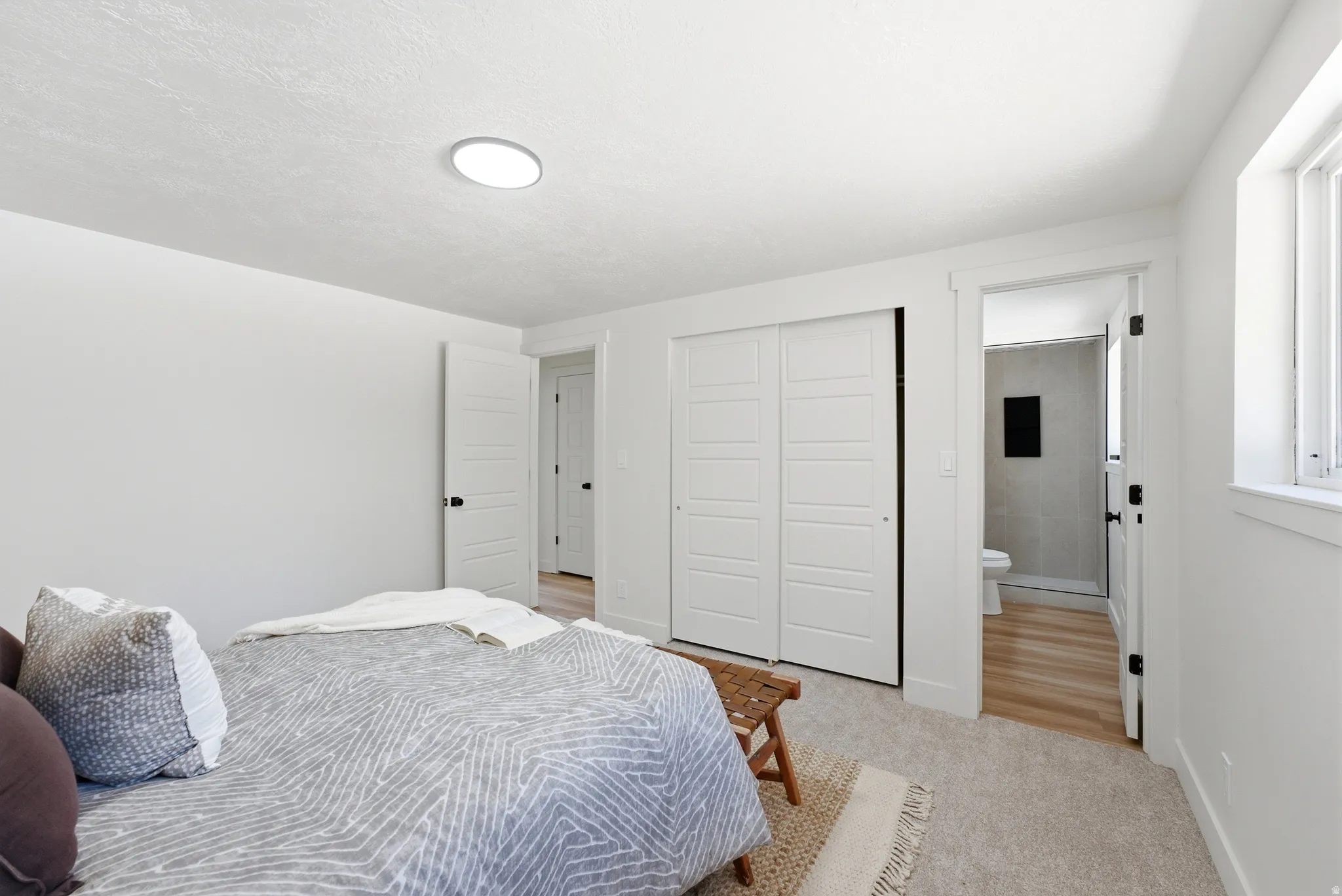 Room featuring light-toned carpeting, a modern flush-mount ceiling light, and white paneled bi-fold closet doors