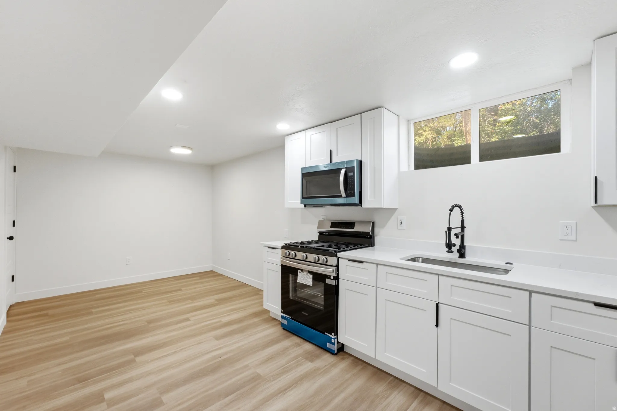 Modern kitchen featuring white shaker cabinetry, quartz countertops, a stainless steel range, and an over-the-range microwave